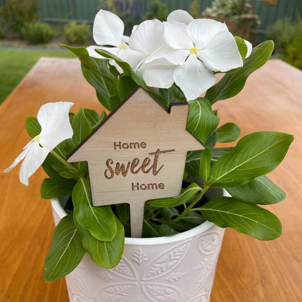 Home Sweet Home planter stick placed in a pot with white flowers